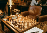 Chessboard set up for a game between two players in a cozy lounge with leather chairs and a fireplace